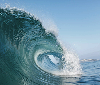 A close-up photo of a curling ocean wave, capturing the dynamic motion and splash of sea water, intelligently connecting viewers to the sheer power of nature, with a clear blue sky in the background